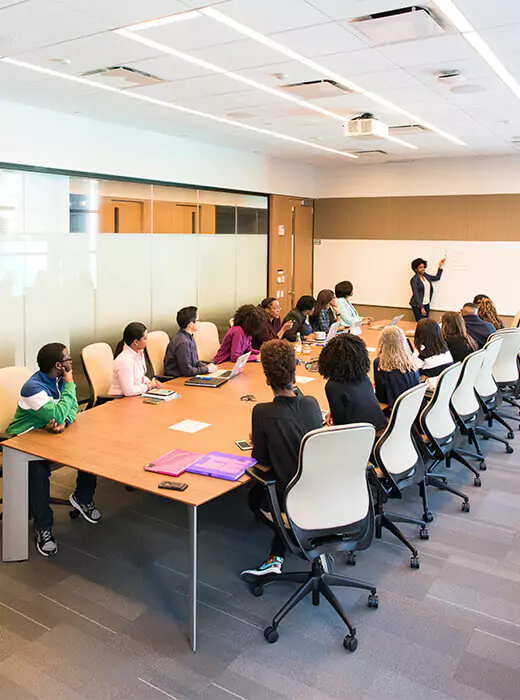 Group of diverse individuals engaged in a collaborative meeting, with a speaker presenting at a conference table in a modern office setting, emphasizing teamwork and creativity.