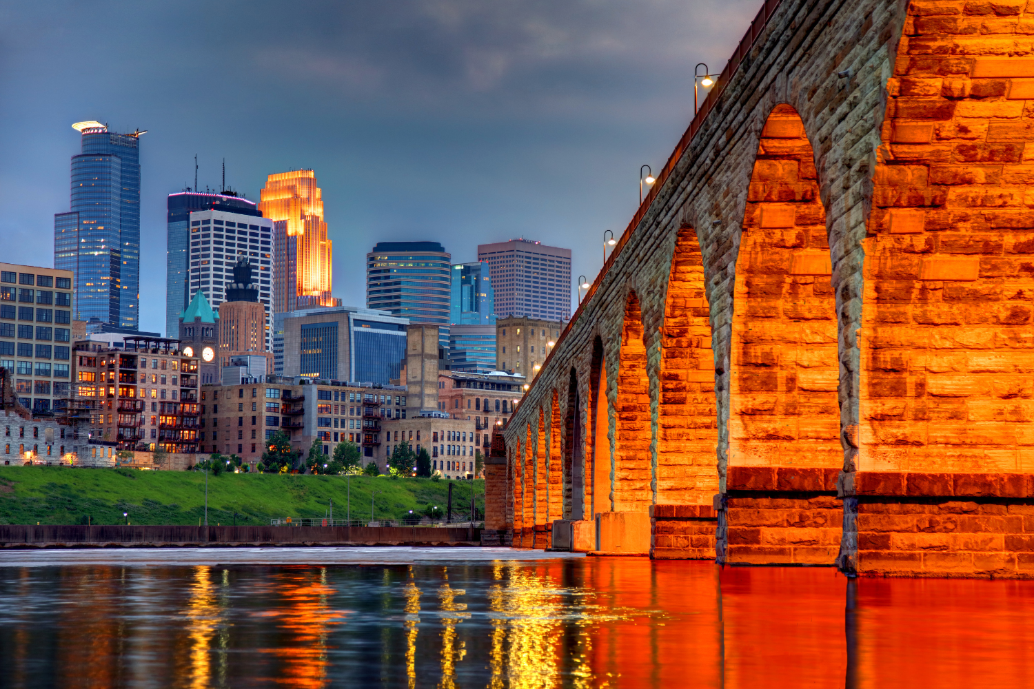 Minneapolis skyline featuring modern skyscrapers and historic stone bridge reflecting in the water, symbolizing the city's blend of creativity and innovation in digital marketing.