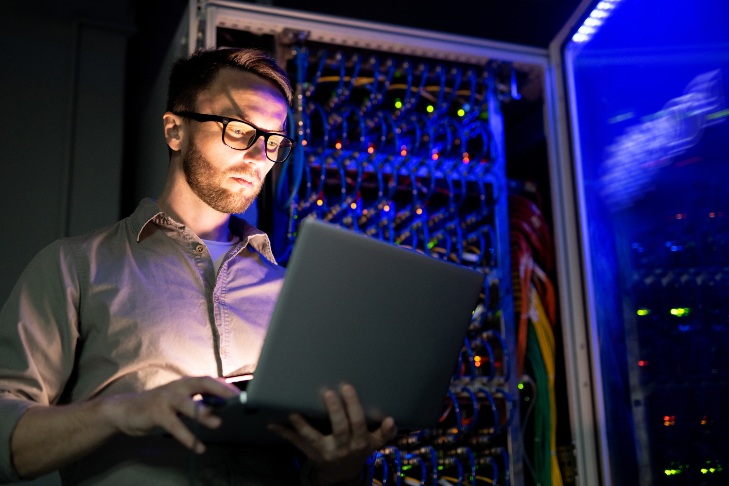 IT professional using a laptop in a server room, analyzing digital marketing data amidst illuminated server equipment, reflecting the focus on tailored digital marketing solutions for IT companies.