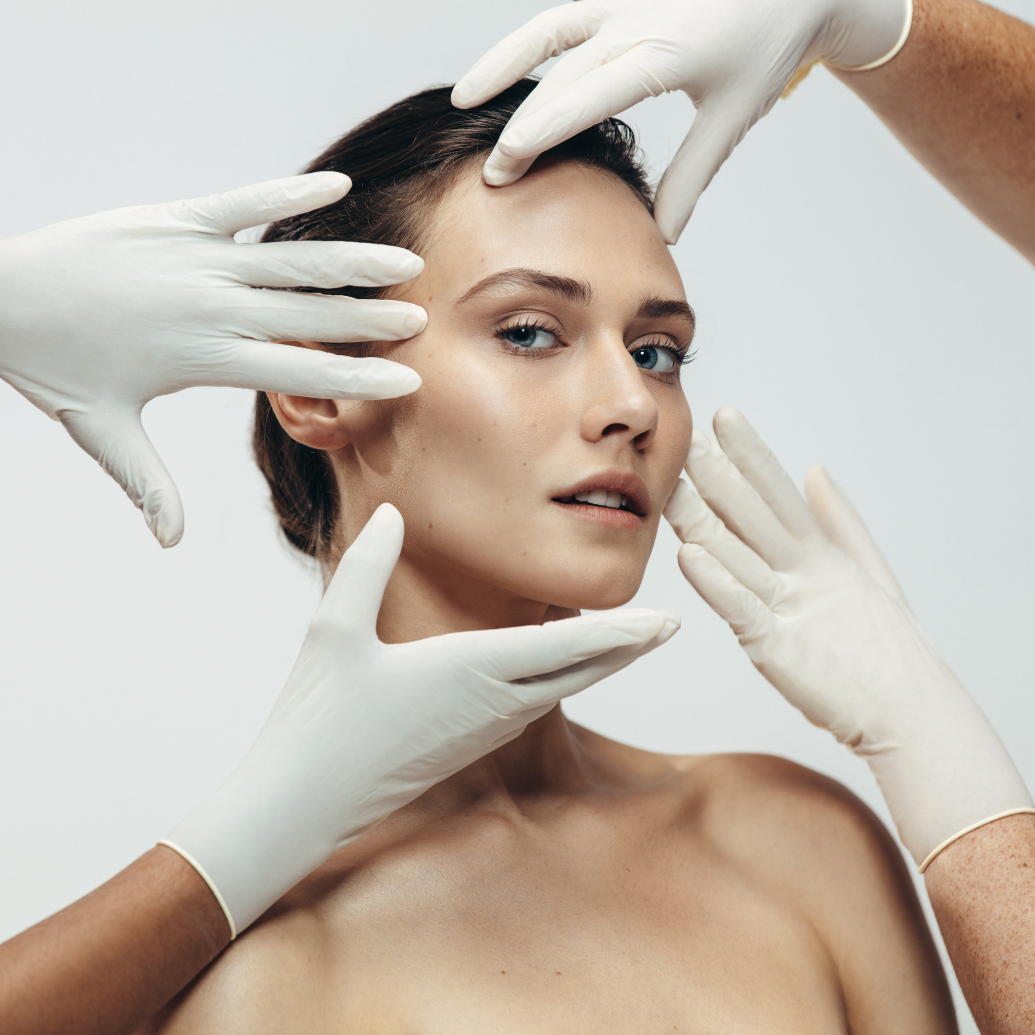 Woman with a natural look surrounded by gloved hands, emphasizing aesthetics and skincare, reflecting professional med spa services.