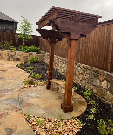 Wooden pergola structure in landscaped garden with stone pathway and greenery, showcasing outdoor design elements for residential spaces.