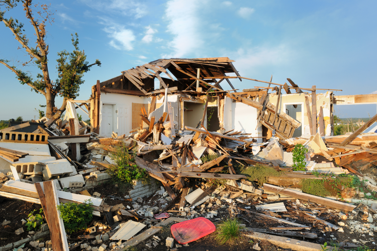 Damaged house debris scattered around a collapsed structure, illustrating the aftermath of a natural disaster, relevant to discussions on supporting tornado victims.