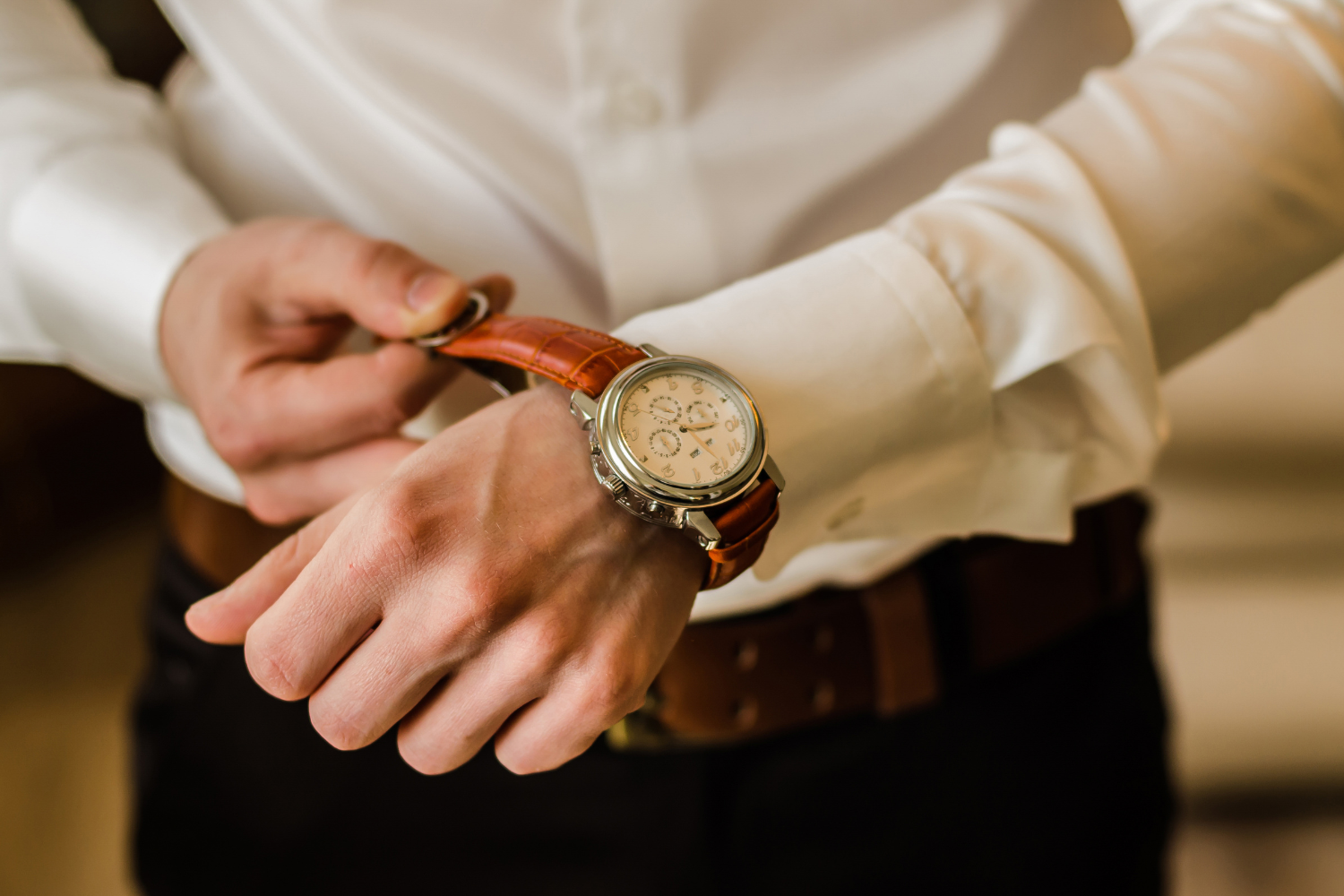 Man adjusting a stylish watch with a brown leather strap, dressed in a white shirt, emphasizing precision and professionalism in the context of selling watches online.