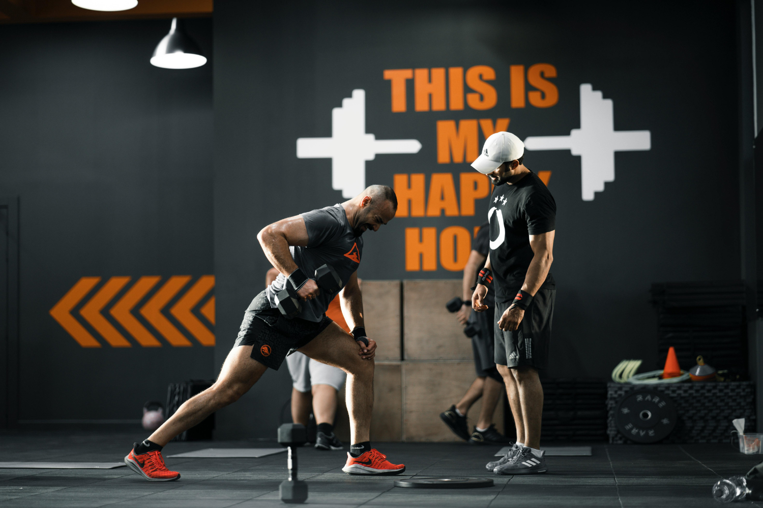 Man performing a dumbbell exercise in a gym, with a motivational wall text "THIS IS MY HAPPY PLACE" in the background, illustrating effective workout environments for gym marketing.