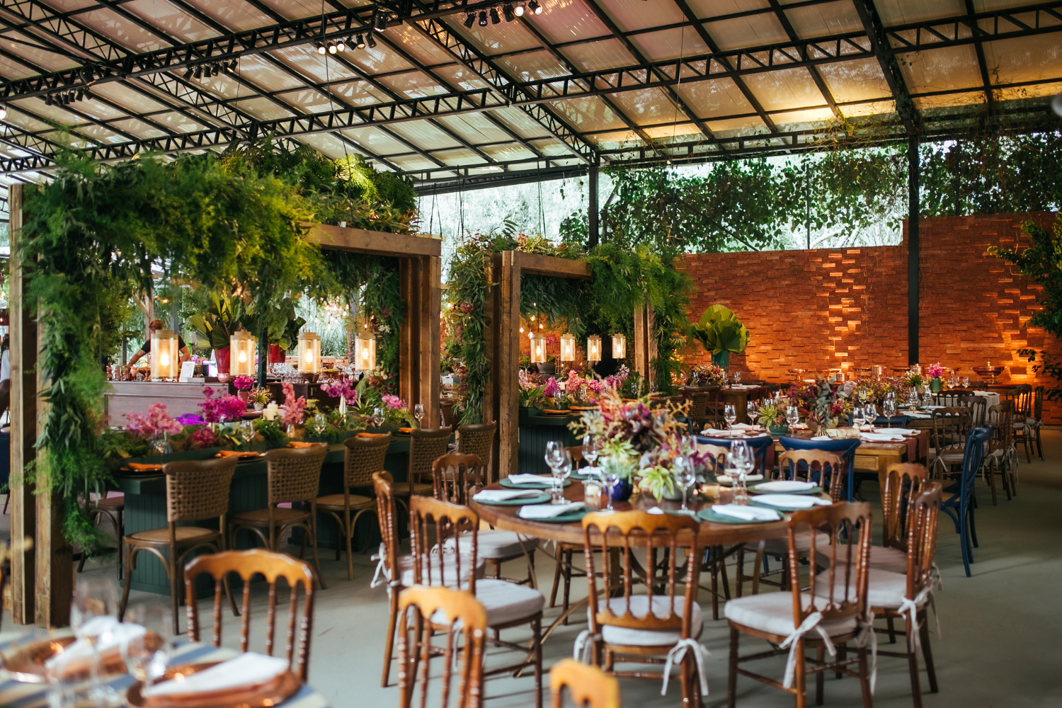Elegant dining setup in a lush indoor venue, featuring wooden tables adorned with floral arrangements and greenery, emphasizing a warm, inviting atmosphere for events.