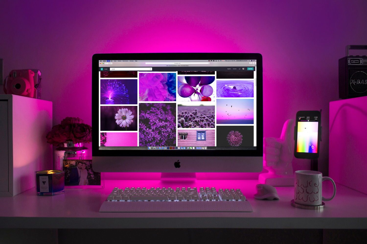 Desktop computer displaying a vibrant collection of purple-themed images, surrounded by decorative items including a candle, flowers, and a smartphone, all set against a softly lit workspace.