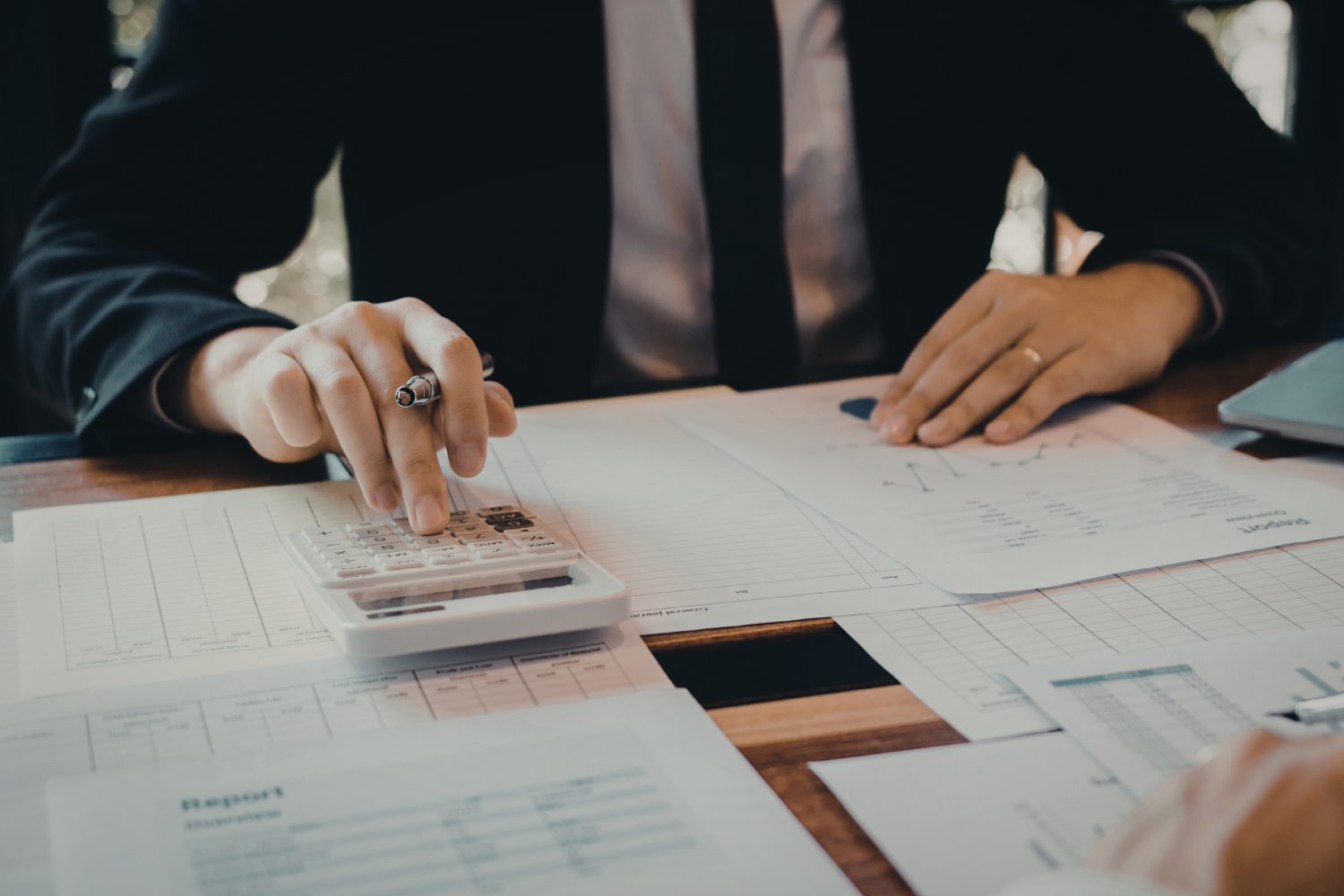 Business professional calculating data on a calculator with financial reports and graphs on a desk, highlighting analytical skills for HVAC marketing strategies.