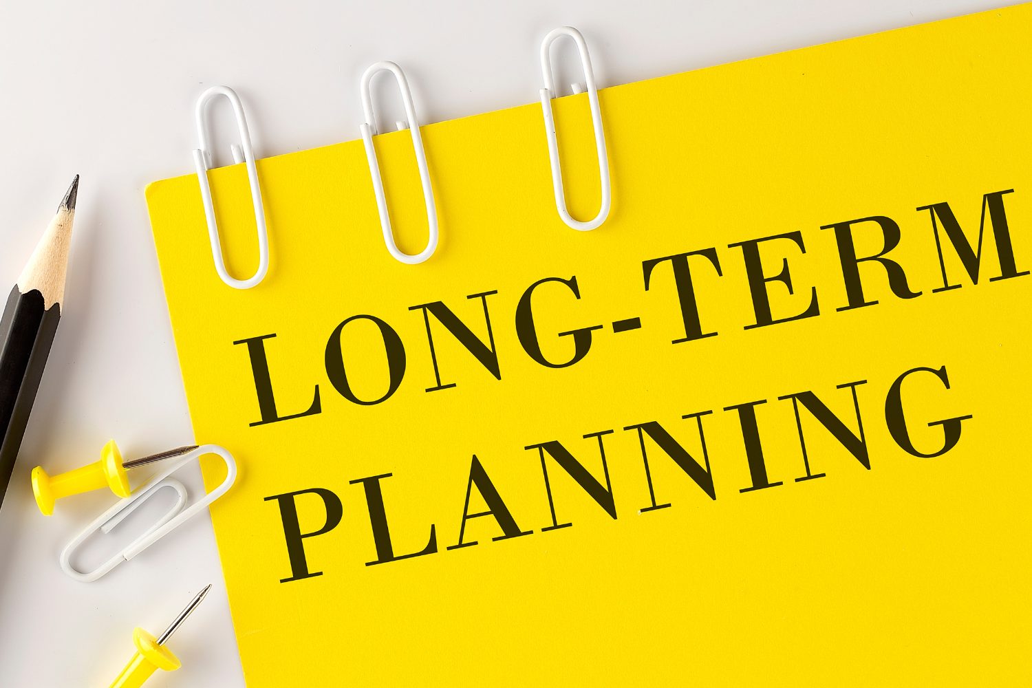 Long-term planning concept illustrated with a yellow notepad featuring bold text, accompanied by stationery items like a pencil, paperclips, and pushpins, symbolizing strategic marketing efforts.