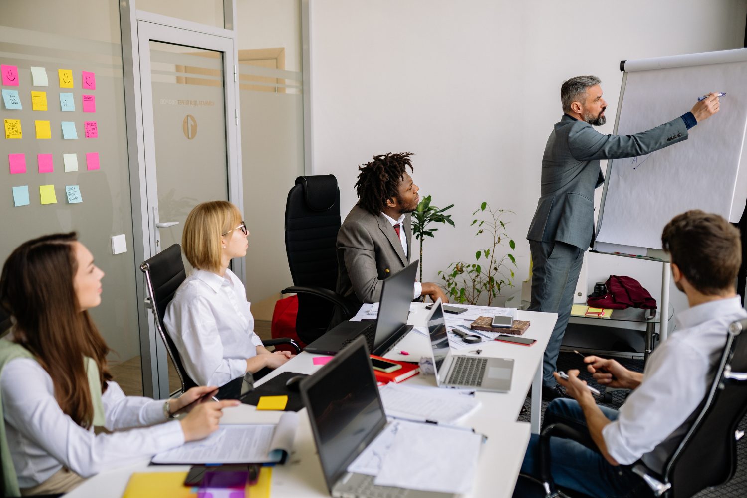 Team meeting in a modern office setting, discussing digital marketing strategies, with a presenter at a whiteboard and laptops on the table.